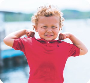 Child Smiling in front of lake with arms raised to show strength