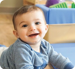 Young child smiling while laying on floor mat in front of box of blocks in child care center classroom